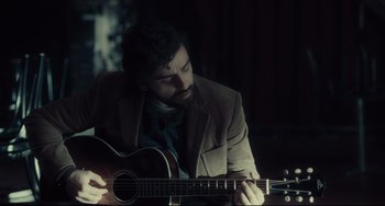 Movie still from “Inside Llewyn Davis” (2013), directed by Ethan Coen – A man in a brown jacket is playing a guitar; Medium shot, Over the shoulder angle