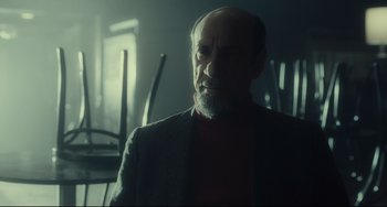 Movie still from “Inside Llewyn Davis” (2013), directed by Ethan Coen – An older man with a beard is standing in a dark room; Medium shot, Over the shoulder angle