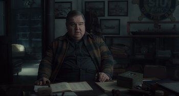 Movie still from “Inside Llewyn Davis” (2013), directed by Ethan Coen – An older man sitting at a table with a book; Medium shot, Over the shoulder angle