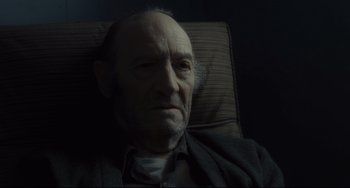 Movie still from “Inside Llewyn Davis” (2013), directed by Ethan Coen – An older man sitting in a chair looking at the camera; Close Up shot, Over the shoulder angle