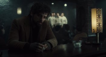 Movie still from “Inside Llewyn Davis” (2013), directed by Ethan Coen – A man sitting at a table in front of a group of men; Medium shot, Over the shoulder angle
