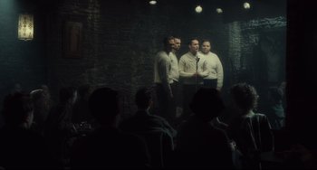 Movie still from “Inside Llewyn Davis” (2013), directed by Ethan Coen – A group of men standing in front of a microphone in a room; Wide shot, Over the shoulder angle