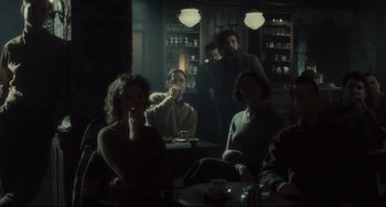 Movie still from “Inside Llewyn Davis” (2013), directed by Ethan Coen – A group of people sitting at a table in a room; Wide shot, Over the shoulder angle