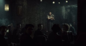Movie still from “Inside Llewyn Davis” (2013), directed by Ethan Coen – A woman standing in front of a microphone in front of a group of people; Wide shot, Over the shoulder angle
