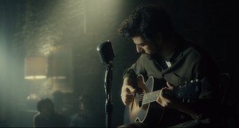 Movie still from “Inside Llewyn Davis” (2013), directed by Ethan Coen – A man playing an acoustic guitar in front of a microphone; Medium shot, Over the shoulder angle