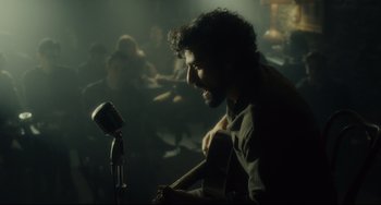 Movie still from “Inside Llewyn Davis” (2013), directed by Ethan Coen – A man sitting in front of a microphone and holding a guitar; Medium shot, Over the shoulder angle