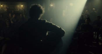 Movie still from “Inside Llewyn Davis” (2013), directed by Ethan Coen – A person sitting in a dark room with a light shining on them; Medium shot, Over the shoulder angle