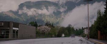 Movie still from “Insomnia” (2002), directed by Christopher Nolan – A car driving down a road near trees and mountains; Extreme Wide shot, High angle