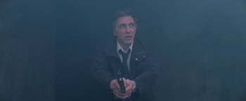 Movie still from “Insomnia” (2002), directed by Christopher Nolan – A man in a black jacket holding a gun in his hands; Medium shot, Low angle