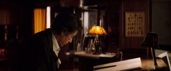 Movie still from “Insomnia” (2002), directed by Christopher Nolan – A man sitting in front of a piano in front of a lamp; Close Up shot, Over the shoulder angle
