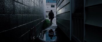 Movie still from “Insomnia” (2002), directed by Christopher Nolan – A person is walking down the street in the rain; Wide shot, Low angle