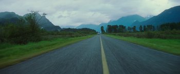 Movie still from “Insomnia” (2002), directed by Christopher Nolan – A car driving down a road near some mountains; Extreme Wide shot, Low angle