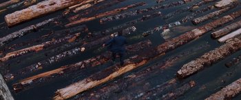 Movie still from “Insomnia” (2002), directed by Christopher Nolan – A man in a blue suit is walking on logs; Extreme Wide shot, Overhead angle