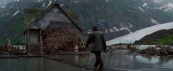 Movie still from “Insomnia” (2002), directed by Christopher Nolan – A man walking across a wet road near a house; Extreme Wide shot, Over the shoulder angle