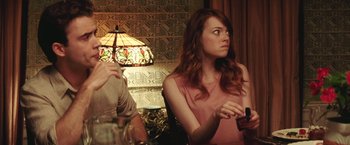 Movie still from “Irrational Man” (2015), directed by Woody Allen – A woman sitting in front of a lamp and a table; Medium shot, Over the shoulder angle