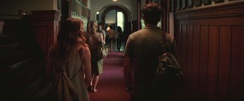 Movie still from “Irrational Man” (2015), directed by Woody Allen – A group of people walking down a red carpet hallway; Medium shot, Over the shoulder angle