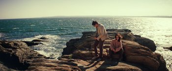 Movie still from “Irrational Man” (2015), directed by Woody Allen – A man and a woman sitting on a rock near the ocean; Wide shot, High angle