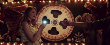 Movie still from “Irrational Man” (2015), directed by Woody Allen – A woman holding up a cell phone in front of a wheel of fortune; Medium shot, Over the shoulder angle