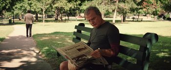 Movie still from “Irrational Man” (2015), directed by Woody Allen – A man sitting on a park bench reading a newspaper; Medium shot, Over the shoulder angle