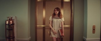 Movie still from “Irrational Man” (2015), directed by Woody Allen – A woman standing in front of an elevator holding a purse; Medium shot, Low angle