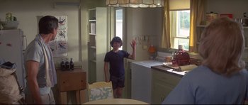 Movie still from “Jaws” (1975), directed by Steven Spielberg – A young man waving in the kitchen of his home; Wide shot, Over the shoulder angle
