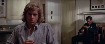 Movie still from “Jaws” (1975), directed by Steven Spielberg – A young man holding a drink in his hand while standing next to another man; Close Up shot, Low angle