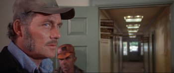 Movie still from “Jaws” (1975), directed by Steven Spielberg – A man with a beard and a hat is looking at another man in a hallway; Close Up shot, Over the shoulder angle