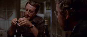 Movie still from “Jaws” (1975), directed by Steven Spielberg – A man in plaid shirt holding a bottle of wine; Close Up shot, Over the shoulder angle