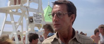 Movie still from “Jaws” (1975), directed by Steven Spielberg – A person wearing glasses near a crowd; Close Up shot, Low angle