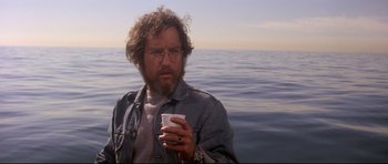 Movie still from “Jaws” (1975), directed by Steven Spielberg – A man holding a cup while standing in front of a body of water; Medium shot, Low angle