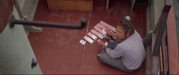 Movie still from “Jaws” (1975), directed by Steven Spielberg – A man sitting on the ground playing a card game; Medium shot, High angle