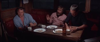 Movie still from “Jaws” (1975), directed by Steven Spielberg – A group of people sitting at a table with plates of food on it; Medium shot, High angle