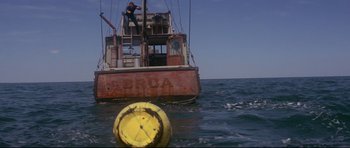 Movie still from “Jaws” (1975), directed by Steven Spielberg – A man standing on the side of a boat in the water; Extreme Wide shot, High angle