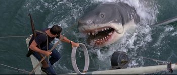 Movie still from “Jaws” (1975), directed by Steven Spielberg – A man holding onto a rope as a large shark approaches him; Wide shot, Overhead angle