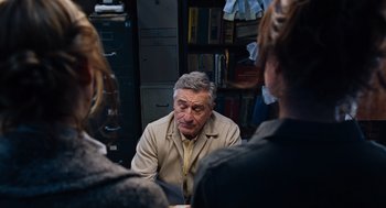 Movie still from “Joy” (2015), directed by David O. Russell – A man sitting in front of two other people; Medium shot, Over the shoulder angle