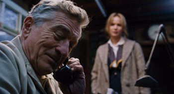 Movie still from “Joy” (2015), directed by David O. Russell – An older man talking on a phone while a woman stands behind him; Close Up shot, Over the shoulder angle