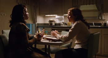 Movie still from “Joy” (2015), directed by David O. Russell – Two women sitting at a table in a kitchen talking to each other; Medium shot, Over the shoulder angle