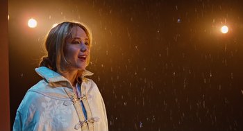 Movie still from “Joy” (2015), directed by David O. Russell – A woman standing in the rain with her mouth open; Medium shot, Low angle