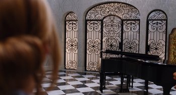 Movie still from “Joy” (2015), directed by David O. Russell – A black and white checkerboard floor with a piano in front of a black and white checkerboard floor; Wide shot, High angle