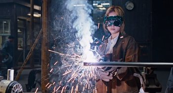 Movie still from “Joy” (2015), directed by David O. Russell – A woman wearing goggles and a welding mask; Medium shot, Low angle