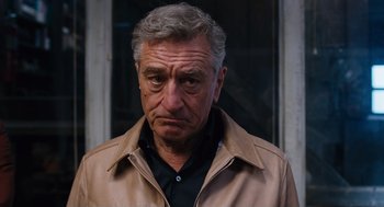 Movie still from “Joy” (2015), directed by David O. Russell – An older man wearing a brown jacket looking at the camera; Close Up shot, Over the shoulder angle