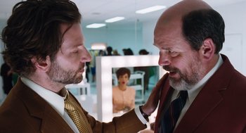 Movie still from “Joy” (2015), directed by David O. Russell – Two men in suits and ties touching each other's hair; Medium shot, Over the shoulder angle