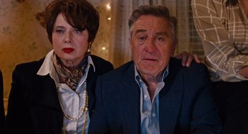 Movie still from “Joy” (2015), directed by David O. Russell – An older man and a younger woman posing for a picture; Medium shot, High angle