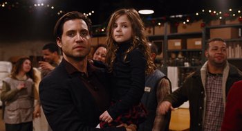 Movie still from “Joy” (2015), directed by David O. Russell – A man holding a little girl in his arms; Medium shot, Over the shoulder angle