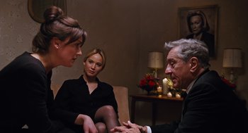 Movie still from “Joy” (2015), directed by David O. Russell – Two women and an older man are sitting in a living room; Medium shot, Over the shoulder angle