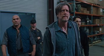 Movie still from “Joy” (2015), directed by David O. Russell – A man standing in front of a group of people; Medium shot, Low angle