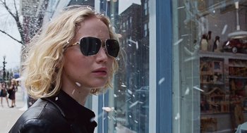 Movie still from “Joy” (2015), directed by David O. Russell – A person wearing sunglasses near a building; Close Up shot, Over the shoulder angle