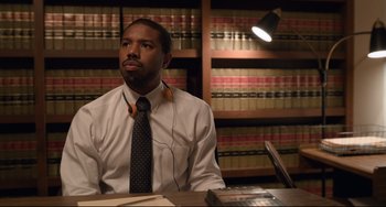 Movie still from “Just Mercy” (2019), directed by Destin Daniel Cretton – A man sitting at a desk in front of a book case; Medium shot, High angle