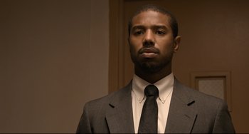 Movie still from “Just Mercy” (2019), directed by Destin Daniel Cretton – A man wearing a suit and tie in front of a wall; Close Up shot, Over the shoulder angle