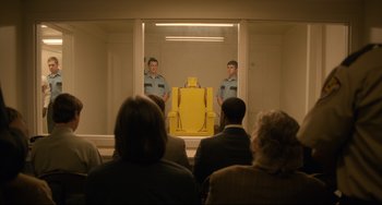 Movie still from “Just Mercy” (2019), directed by Destin Daniel Cretton – Two men standing in front of a yellow chair in front of a group of onlookers; Wide shot, Over the shoulder angle